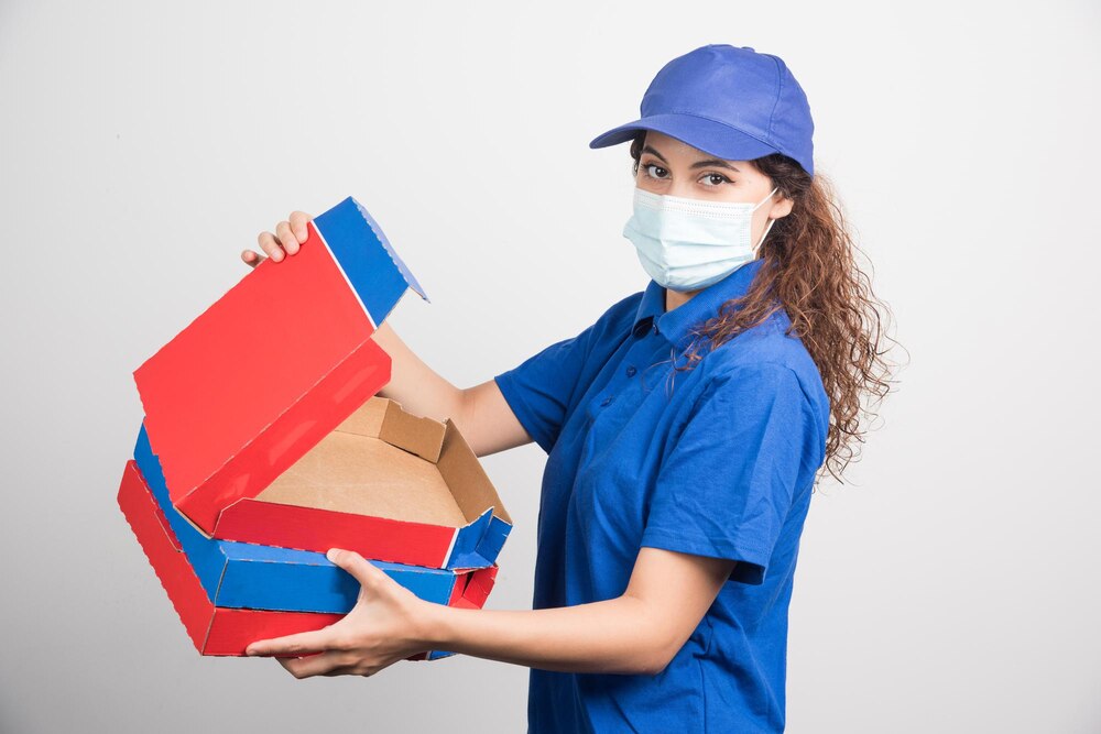 Pizza delivery girl opening one of the boxes of pizza with medical facemask on white